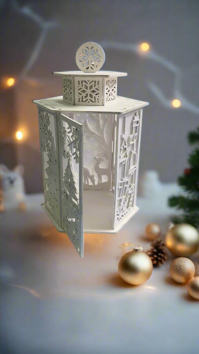 A white tea light candle holder with a Christmas tree and snowflake design, placed on a surface with a blurred Christmas tree and decorations in the background.
